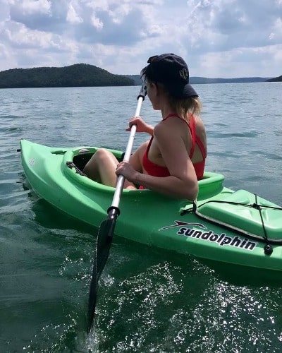 Picture of Alyson Acklin boating in a lake in a orange bikini dress with a black cap